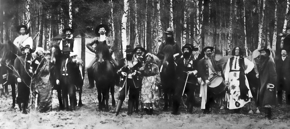 En grupp människor i historiska kläder står och sitter på hästar i en skog, svartvit bild.