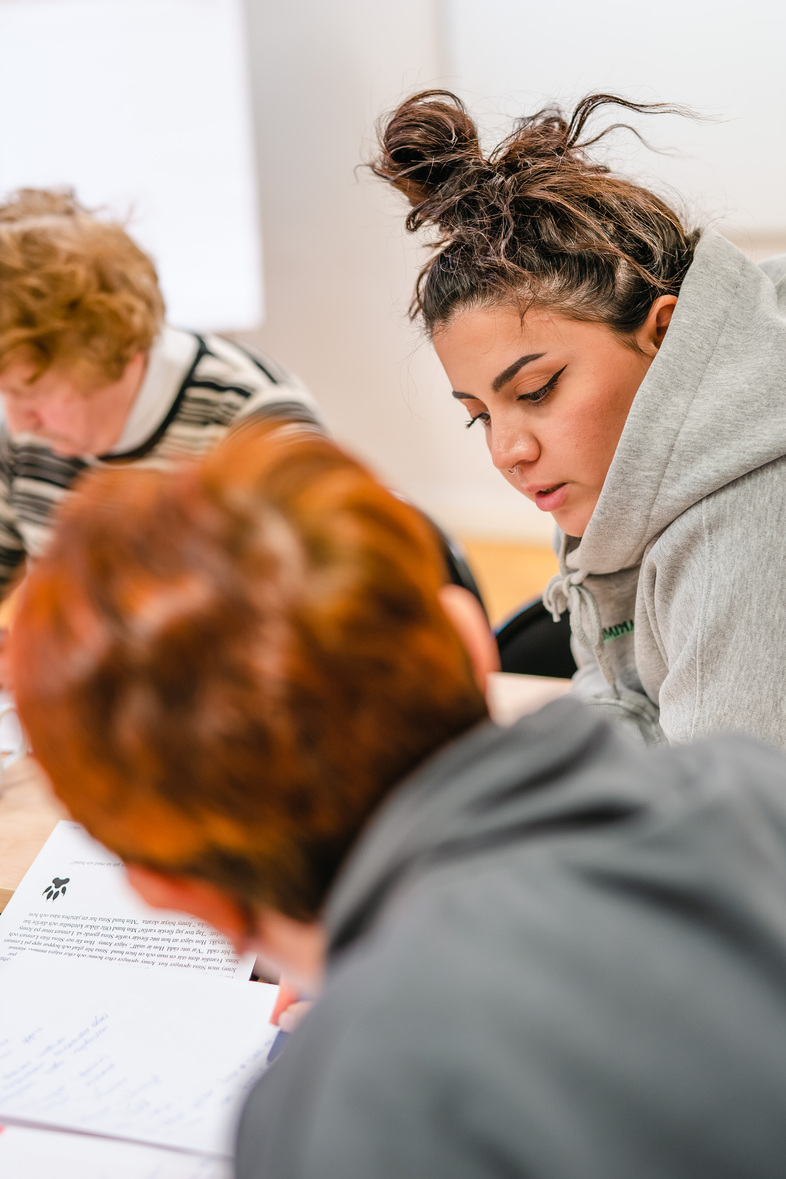 Två unga personer sitter vid ett bord och arbetar tillsammans med papper och penna.