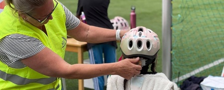 En vuxen hjälper ett barn att ta på en cykelhjälm på en idrottsplats utomhus.