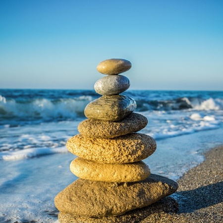 Stapel av stenar på en sandstrand med havsvågor i bakgrunden under klarblå himmel.
