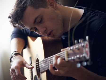 Ung man spelar akustisk gitarr och tittar koncentrerat på strängarna.
