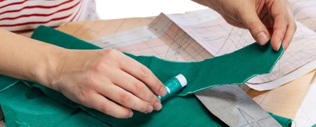 En person markerar tyg med krita, omgiven av mönsterpapper, sax och måttband på ett bord.
