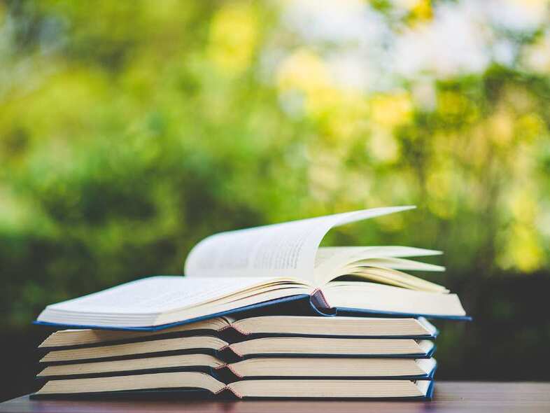 En trave uppslagna böcker på ett bord utomhus.