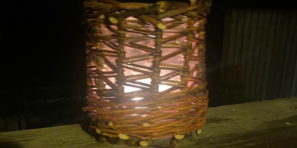 En flätad lykta med ett tänt ljus inuti står på ett trästaket i mörkret.