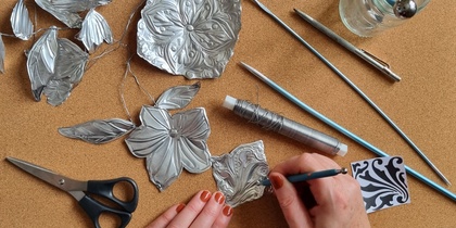 En person arbetar med metallprägling och formar blommor och blad av tunn metall på en korkmatta.