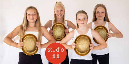 Fyra unga tjejer i vita linnen och svarta byxor håller gyllene hattar framför sig, står mot vit bakgrund.