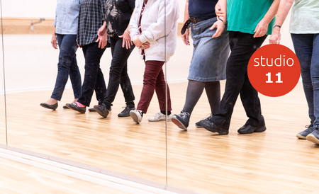 Sex personer övar danssteg framför en spegel i en dansstudio, endast benen syns.