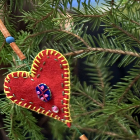 Röd filtdekoration i form av ett hjärta hänger i en grön julgran.