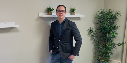 En person står vid väggen i ett mötesrum med bord, stolar, växter och hyllor med krukväxter.