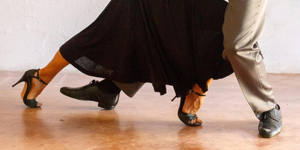 Ett par dansar tango i en elegant pose mot en ljus vägg.