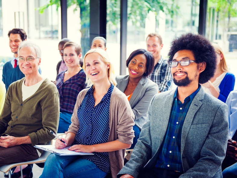 En grupp människor sitter och ler under en föreläsning eller workshop i ett ljust rum.