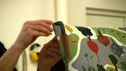 En person syr eller lagar ett kuddfodral med färgglatt grönsaksmönster.