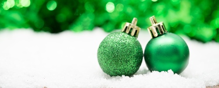 Två gröna julgranskulor står på konstsnö med suddig grön bakgrund.