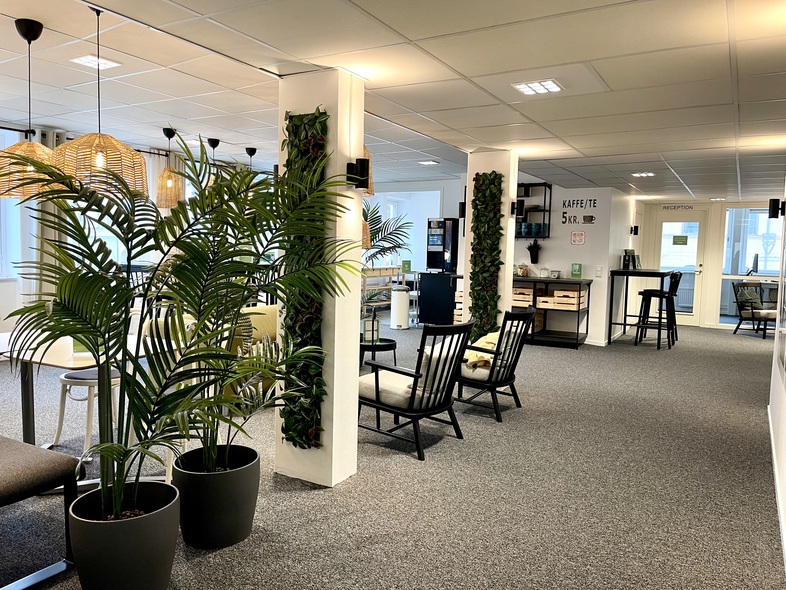 Modernt kontorsutrymme med gröna växter, sittgrupper och ljusa färger.