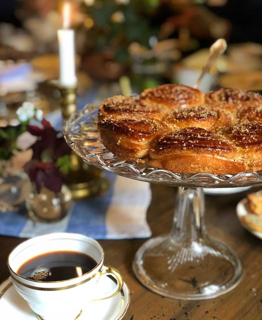 Kaffekopp och kanelbullar på ett fat, dukat bord med levande ljus och blommor.