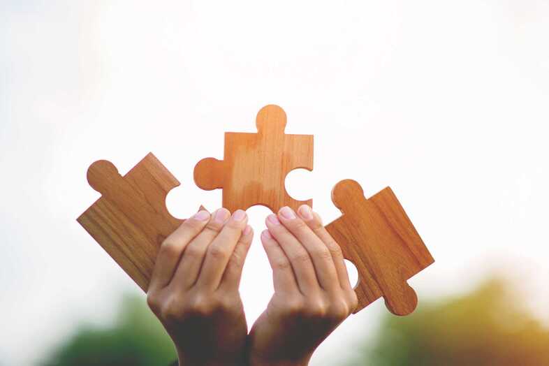 Två händer håller i tre stora puzzelbitar av trä.