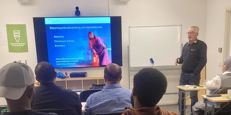 Föreläsning om brandsäkerhet i ett klassrum med deltagare och en presentatör vid en stor skärm.