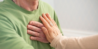 Två händer placerade på bröstet av en person i grön tröja, som en gest av stöd eller hjälp.