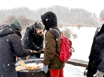 Fyra personer står runt en eld utomhus i ett snöigt vinterlandskap, klädda i vinterkläder.