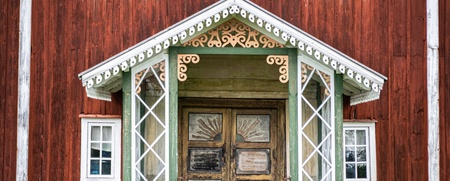 Entré till ett rött trähus med snickarglädje, gröna detaljer och dubbeldörrar i trä.