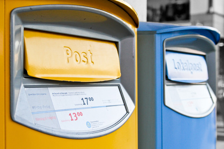 Två postlådor, en gul och en blå, står bredvid varandra utomhus. Texten 'Post' och 'Lokalpost' syns tydligt.