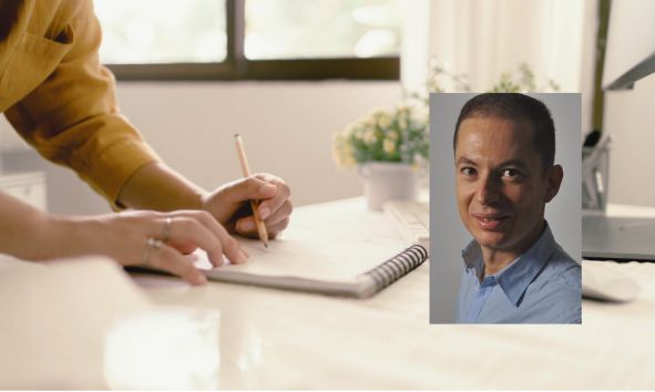 Person skriver i anteckningsbok på ett ljust kontor med växter och fönster i bakgrunden.