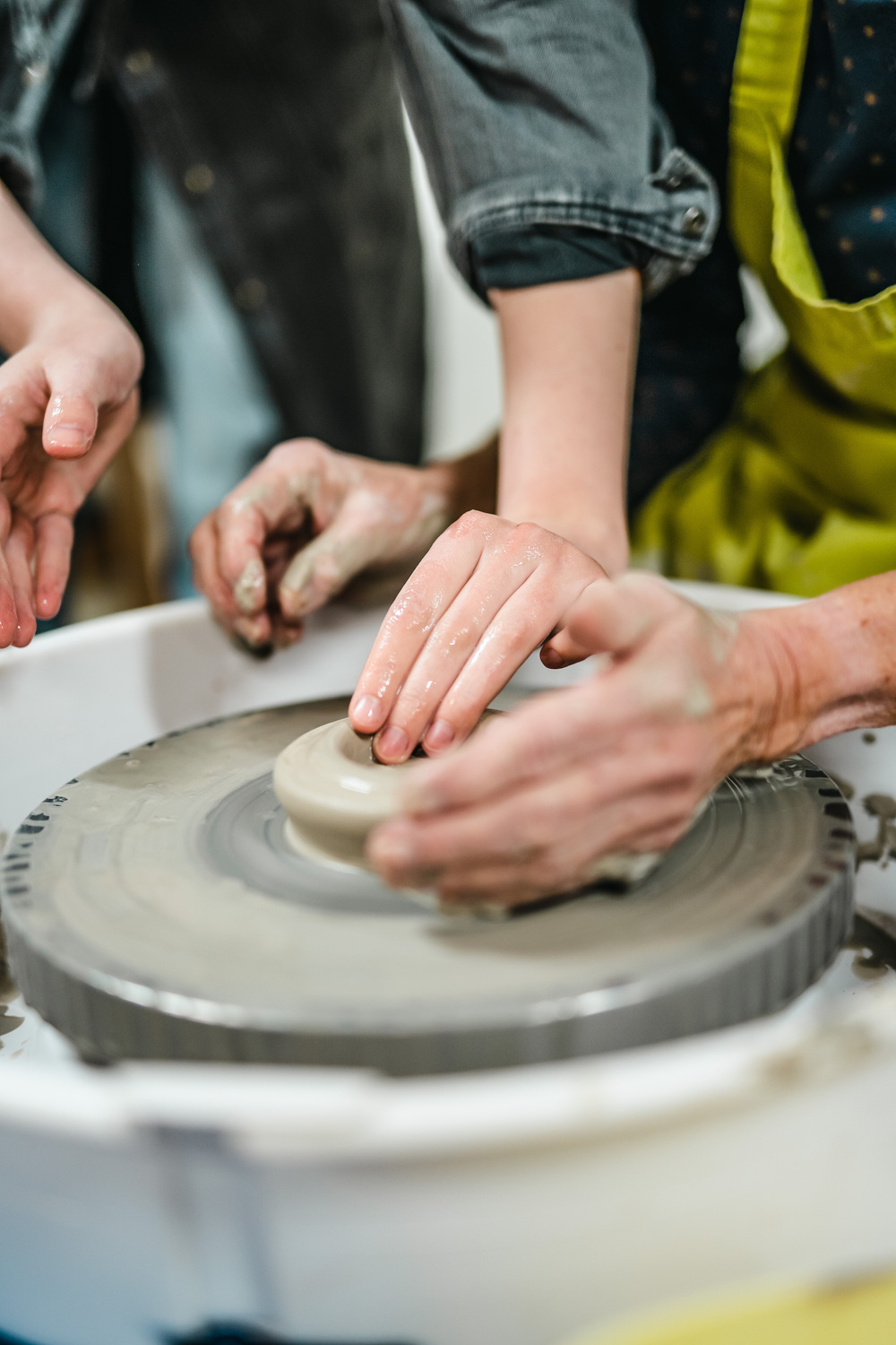 Två personer formar lera på en drejskiva med sina händer i en keramikverkstad.