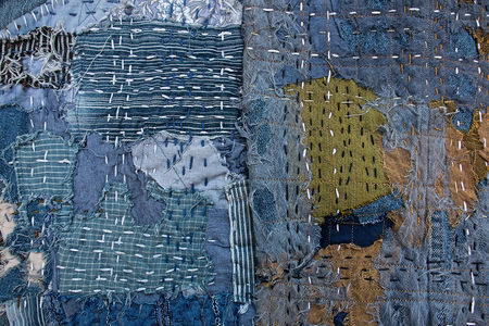 Närbild av lappad textil med synliga stygn i blå, gröna och bruna nyanser.