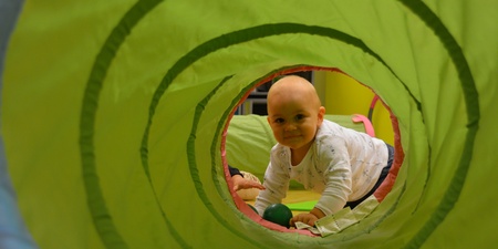 Ett litet barn kryper genom en grön lektunnel och tittar mot kameran.