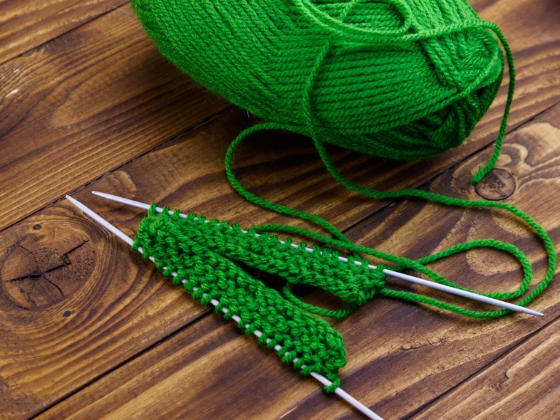 Grönt garnnystan och stickning på träbord med två stickor och påbörjat arbete.