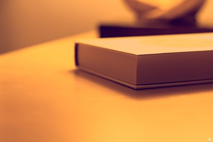 En bok ligger stängd på ett bord i varmt, gulaktigt ljus.