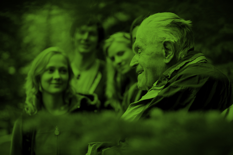 En äldre man samtalar med tre yngre personer utomhus, bilden har ett grönt filter.
