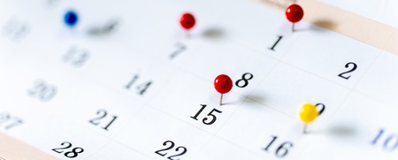 Närbild av en kalender med färgade nålar som markerar viktiga datum.