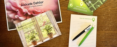 Böcker, block och pennor om folkbildning och kulturväxter ligger på ett träbord.