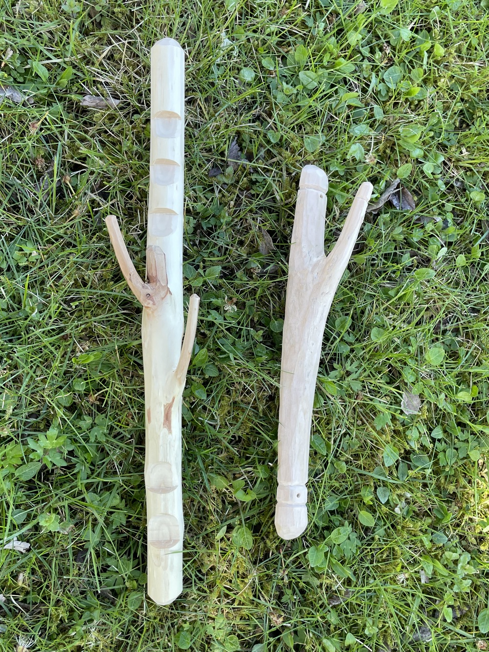 Två Y-formade träpinnar ligger på gräs, täljde och bearbetade för hand.