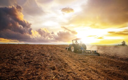 En traktor plöjer en åker vid solnedgången under en dramatisk himmel.