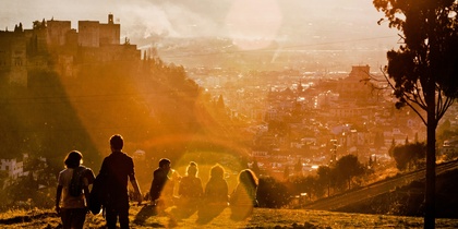 En grupp människor går i motljus på en kulle med utsikt över en stad och en borg i solnedgången.