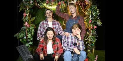 Fyra personer i rutiga skjortor poserar framför en blomsterdekorerad bakgrund, två sitter och två står bakom.