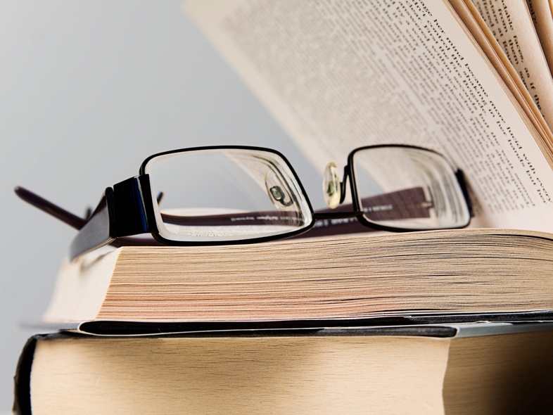 Ett par glasögon ligger ovanpå en öppen bok med en annan bok under.