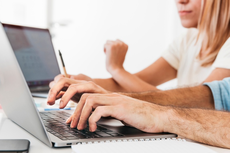 Två personer arbetar vid en bärbar dator med anteckningsblock och mobiltelefon på ett vitt skrivbord.