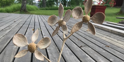 Träskulptur av två blommor på en träplatta, placerad på ett trädäck utomhus.