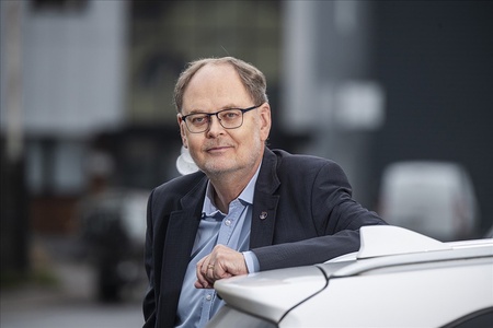 Clas Svahn lutar sig mot en vit bil utomhus i stadsmiljö.