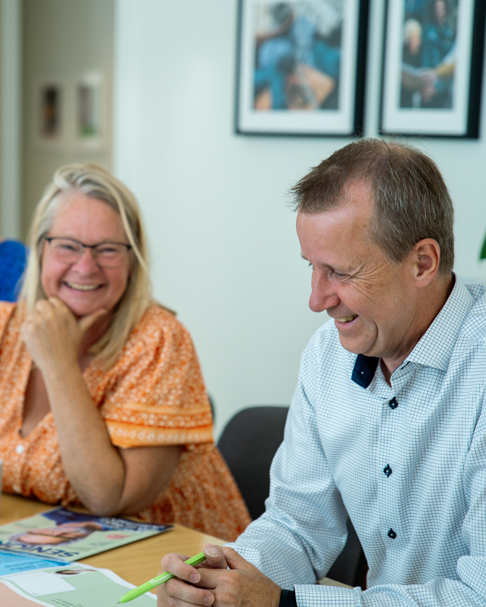 Två glada personer sitter vid ett bord och samtalar i ett ljust kontorsrum.