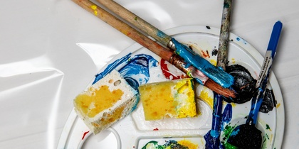 En konstnärspalett med färgglada färger, penslar och svampar på en vit bakgrund.