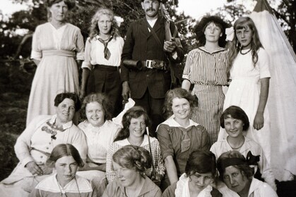 Svartvit gruppbild på unga kvinnor och en man utomhus, klädda i tidstypiska kläder från tidigt 1900-tal.