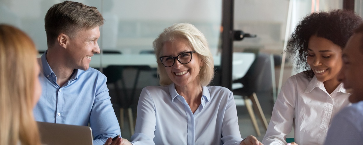 Fyra personer sitter runt ett bord på ett kontor och har ett glatt möte.