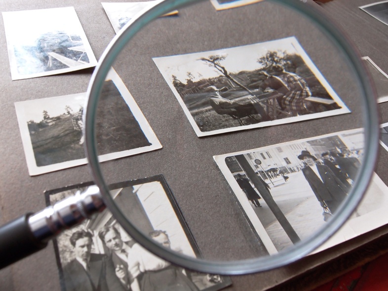 Ett fotoalbum med svartvita fotografier granskas med ett förstoringsglas.