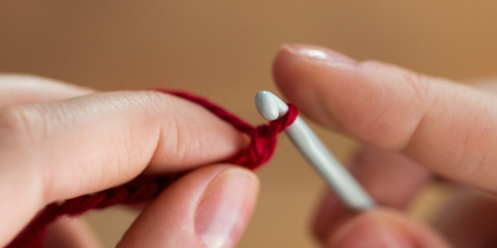 Närbild av händer som virkar med röd garn och en virknål.