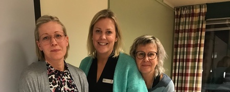 Fyra kvinnor poserar tillsammans i ett mötesrum med stolar och bord i bakgrunden.