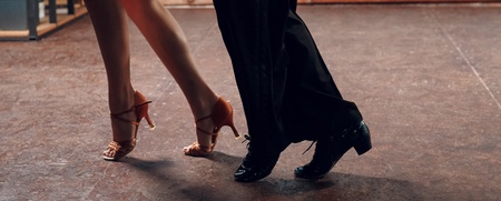 Två personer dansar tillsammans på ett golv, endast deras ben och fötter syns.
